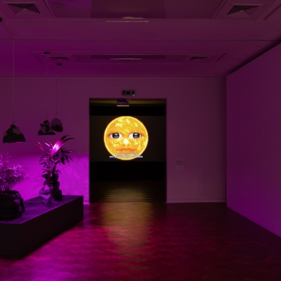 Widok na wystawę "Zwichnięty czas", fot. A. Zagrodzka: przestszeń wystawy, w środku jest dzieło sztuki przedstawiające słońce. A w pokoju jest fioletowe światło