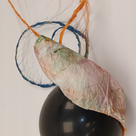 Abstrakcyjna rzeźba o organicznej formie. Centralnym elementem jest nadmuchany balon, który owinięty jest delikatnym, pogniecionym papierem. Na górze jest umocowana abstrakcyjna konstrukcja z cienkich, kolorowych nici, tworząca wrażenie delikatnej sieci lub pajęczyny.