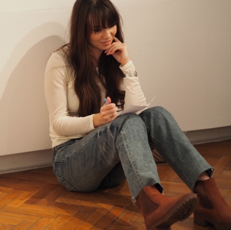 A young girl sits on the floor. He leans against the wall.
