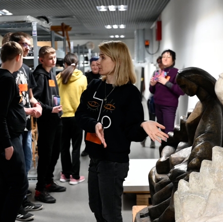 A person standing in front of the audience pointing with his hands at the sculptures standing nearby