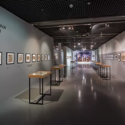 Zdjęcie przedstawia przestrzeń wystawy "Leopold Buczkowski. Przebłyski historii, przelotne obrazki". Na ścianach, po prawej i lewej stronie wiszą grafiki w ramach.