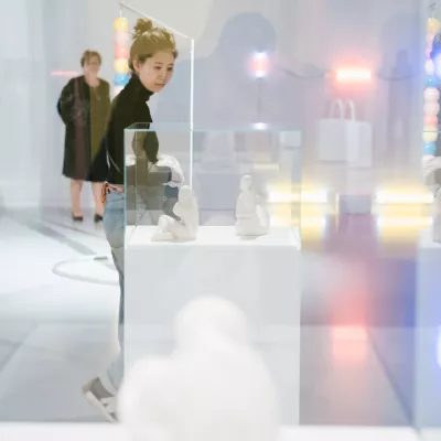 Młoda kobieta w przestrzeni wystawy, patrzy na rzeźbę, która znajduje się w szklanej gablocie