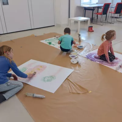 Troje dzieci na wielkich płachatach papieru maluje swoje obrazki