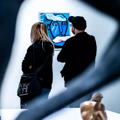 Dwie osoby stoja przed obrazem przedstawiającym twarz namalowaną na niebiesko.