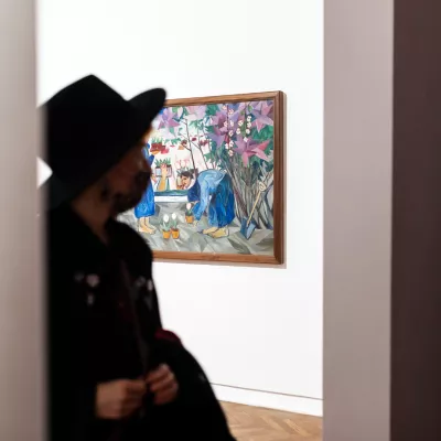 Na zdjęciu kobieta w kapeluszu przechodzi przez sale wystawy, w tle widoczny obraz z kobietami zbierającymi kłosy.