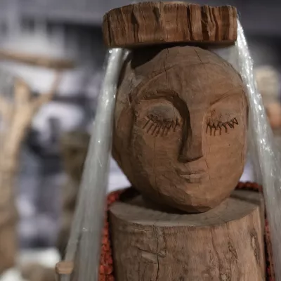 Zdjęcie przedstawia drewnianą rzeźbę, kobietę z zamkniętymi oczami, z nakryciem głowy ozdobionym srebrną lametą