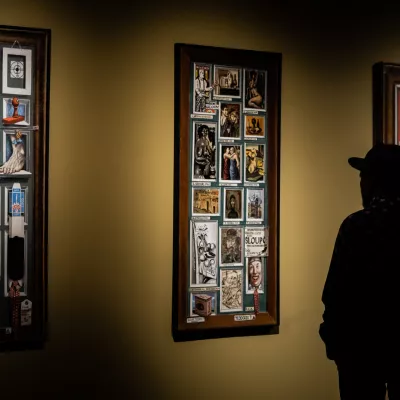 Przestrzeń wystawy "Jerzy Krawczyk. Myszy i ludzie". W pomieszczeniu panuje półmrok, na środku trzy obrazy przed nimi stoi mężczyzna w kapeluszu
