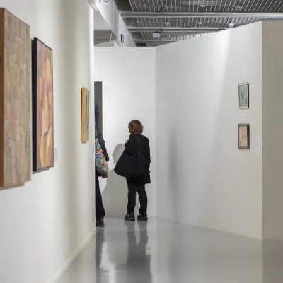 Two people in the exhibition space, paintings hung on white walls